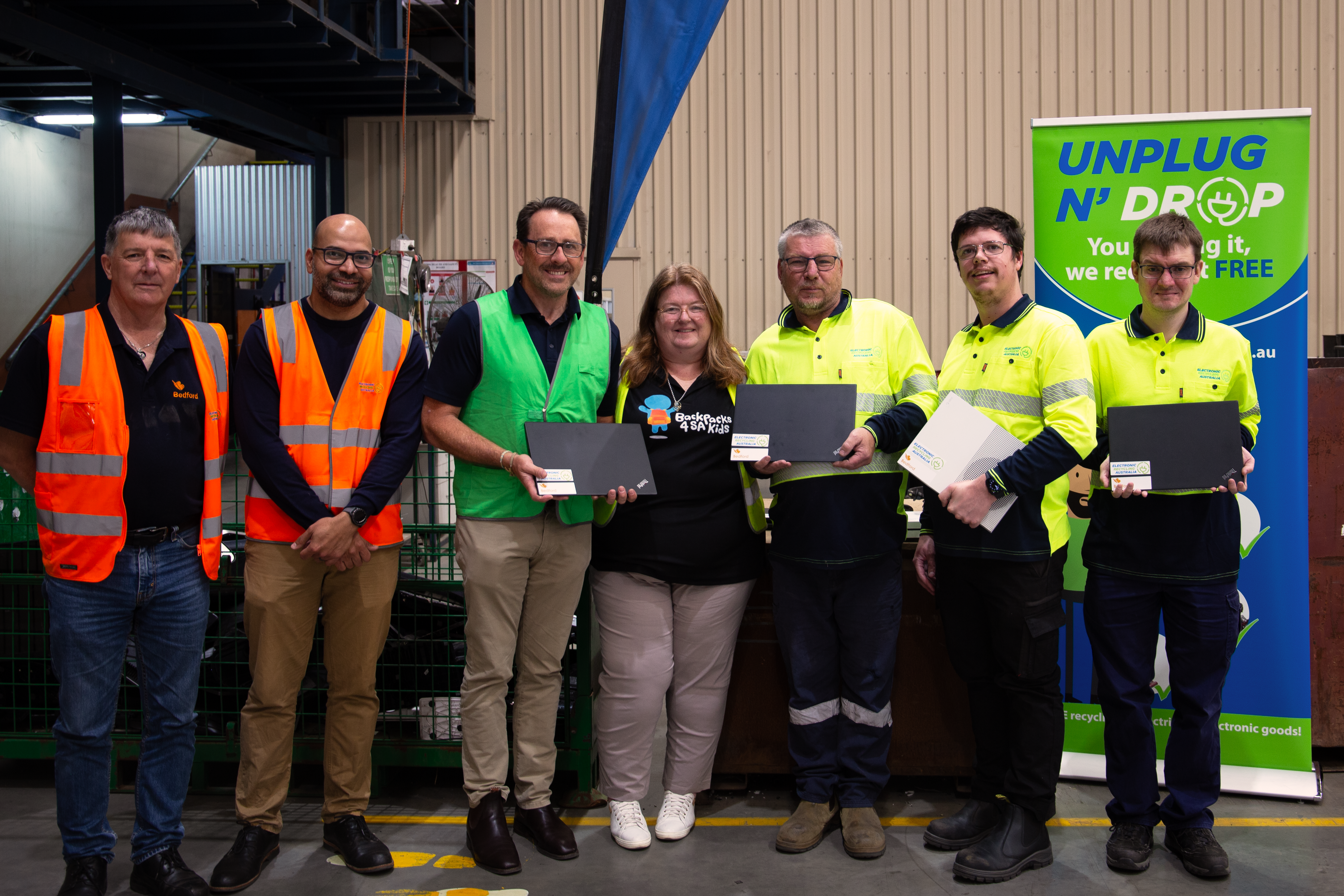 A group of people wearing hi-vis vests standing, with three of them holding laptops.